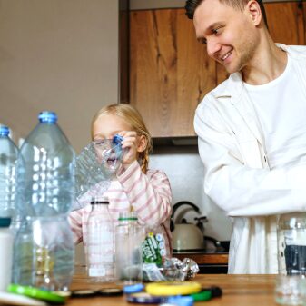 A parent and child sorting plastic bottles and containers at a kitchen table